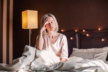 Tired person sitting on bed at home