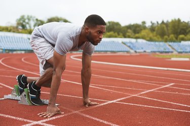 Fit afro-american runner in starting position on stadium