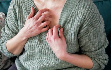 Close up of person in green knit sweater scratching their neck because they have itchy skin all over