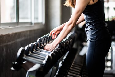 a close up of a young adult using grip strength to lift a dumbbell off a rack of weights at a gym