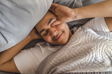 a person rubbing their eyes while lying in bed at home