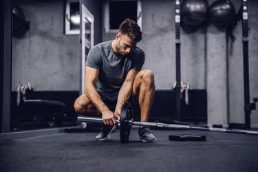 young caucasian man setting up a barbell for a landmine leg workout in the gym.