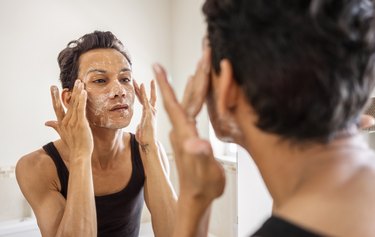 Reflection of person washing face with foam in bathroom