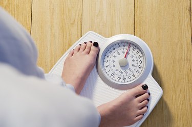 overhead photo of an adult's feet with painted toenails standing on a white bathroom scale