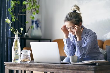 A young professional working from home on their laptop appearing to be tired pressing their temples.