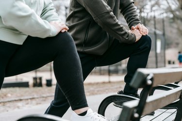 a close up of two people's lower bodies stretching their legs on a park bench