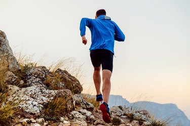 back runner man athlete running uphill trail over stones